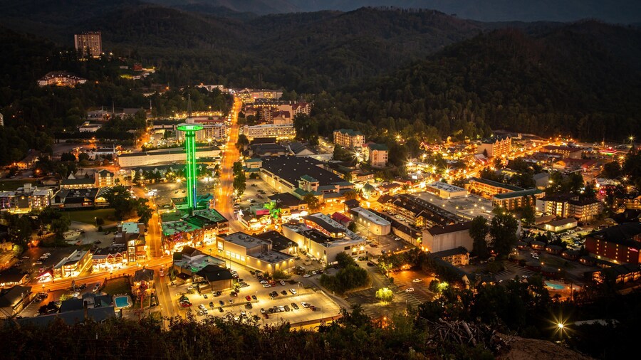 Nighttime view of Gatlinburg Space Needle with city lights and Smoky Mountain backdrop.